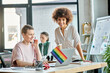 © Bliss - Attractive diverse businesswomen working together on project in office, pride flag.