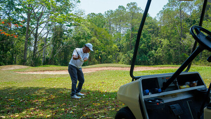 Wall Mural - Golfer plays golf on the fairway with golf cart in the evening at sunset background.