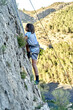 A boy is scaling a steep cliff, clinging to the rock wall as she practices climbing in extreme mountain terrain