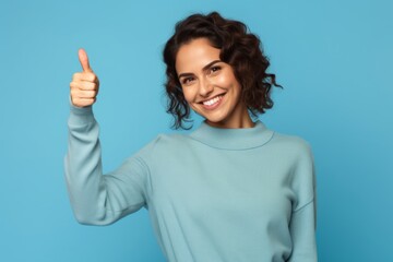 Wall Mural - Portrait of a tender woman in her 30s showing a thumb up isolated in pastel blue background