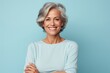 © Markus Schröder - Portrait of a smiling woman in her 50s with arms crossed isolated on pastel blue background