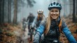 © Sergey - Smiling young woman in cycling gear enjoying a mountain bike ride in a misty forest with friends trailing behind.