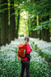 Woman tourist with red backpack hiking in flowering forest. Hike and joy in nature. Female hiker walks in woodland