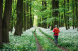 Woman with red backpack hiking in flowering forest. Hike in nature. People and leisure activity outdoors