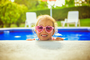 Wall Mural - Smiling cute little girl in sunglasses in pool in sunny day.