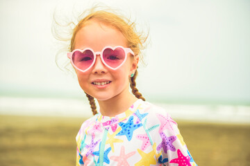 Wall Mural - Portrait of laughing girl of 4 years with heart-shaped sunglasses on beach of Costa Rica