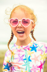 Wall Mural - Portrait of laughing girl of 4 years with heart-shaped sunglasses on beach of Costa Rica