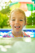 Smiling cute little girl in sunglasses in pool in sunny day.