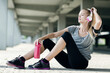 Young woman resting after outdoor workout with headphones and water bottle