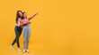 © Prostock-studio - Mother and daughter dressed in casual wear, stand closely together against a vibrant yellow backdrop, pointing at copy space while they both smile brightly, sharing a lighthearted moment.
