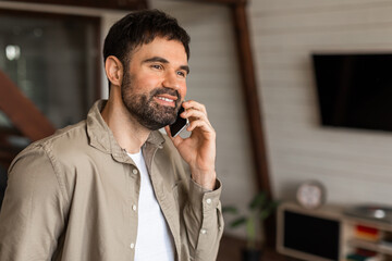 Poster - Closeup of man is standing in a living room, holding a cell phone to his ear, engaged in a phone conversation. The room is furnished with a sofa, coffee table, and lamp.
