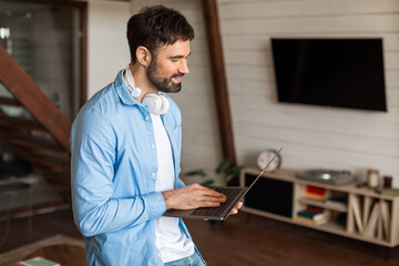 Aufkleber - A man is standing in a living room, focused on using a laptop. The room is well-lit, with furniture in the background. The man appears engaged in his work on the computer.