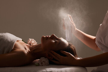 cosmetologist sprays a refreshing spray on a girl’s face on a white background