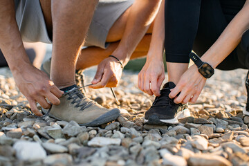 Close up view of hands of athletic man in white t-shirt and woman in black top tying shoelaces before exercising on roof terrace.