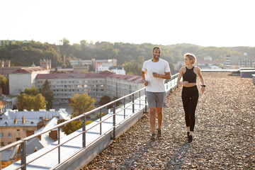 Wall Mural - Young strong female and male athletes engaged in sports running against background of morning city. Happy sporty couple promotes healthy lifestyle.