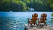 © Chingiz - Two Adirondack chairs are positioned on a wooden dock, facing a serene, blue lake
