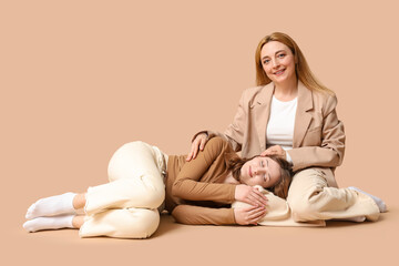 Wall Mural - Beautiful young woman lying on her mature mother's knees brown background. Mother's Day celebration