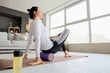Sporty young woman with foam roller doing yoga on mat at home