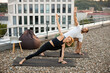 Happy couple doing sports at sunrise on the roof of a modern building. Sports family, husband and wife standing in yoga pose on mats with arms raised up against urban background.