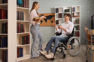 Wall Mural - Male graduate in wheelchair talking to his friend with books at library