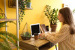 © Pixel-Shot - Young woman working with laptop at table near yellow wall in office