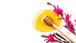 Honey dripping, pouring from wooden honey dipper spoon, isolated on white background. Close-up. Healthy organic liquid honey spill, decorated with gaura flowers. Top view, from above