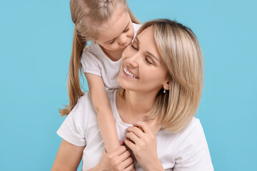 Wall Mural - Daughter kissing her happy mother on light blue background