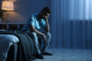 Frustrated man sitting on bed at night