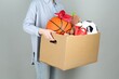 © New Africa - Woman holding box of unwanted stuff on grey background, closeup
