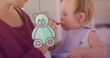 Image of teddy bear icon over caucasian mother feeding her baby with spoon