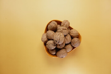 Wall Mural - stack of natural walnuts in a bowl on orange color background 