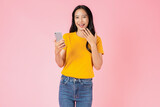 Fototapeta  - Beautiful Asian woman holding smartphone and smiling on pink background.