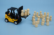 Yellow forklift truck and many wooden people figures on blue background. Strike and meeting concept.	