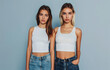 Two beautiful female models in their early twenties, one with long brown hair and the other with short blonde hair, wearing a white tank top and blue jeans