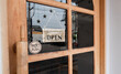Wooden sign hangs welcome open coffee shop door.