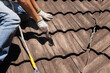Worker man using waterproof roof coating repair to fix crack of the old tile roof.