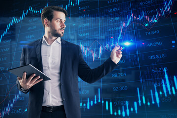 Wall Mural - Attractive young european businessman with tablet using creative candlestick forex chart with index on blurry office background. Trade and stock exchange concept. Double exposure.