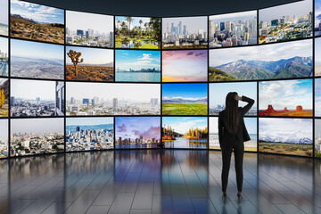 Poster - Back view of young businesswoman looking at video wall in television production room as technology concept with colorful screens and various images. Monitors on light rooms with reflections on floor.