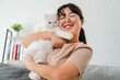 © Suriyawut - A woman is holding a white cat and smiling in the living room at home.