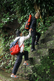 Fototapeta  - Young Man Helping Girlfriend To Climbing Up The Stairs. Hiking in The Forest. 