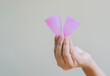 Two pink silicone menstrual cups on woman's hand over light beige background with copy space.