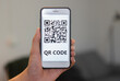Unrecognizable man's hand holding modern smartphone with QR code on screen.