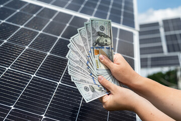 Wall Mural - Saves money with green electricity, hand holding dollar bills against solar panels