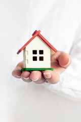 A woman dressed in a white shirt holds a small house in front of her