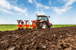 Red tractor plows through fertile soil with a vibrant green landscape in the background