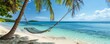 A hammock sways between tall palm trees on a sandy beach, overlooking crystal-clear waters and blue skies, serene landscape
