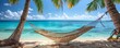 Idyllic hammock scene between palm trees on a beach, facing the clear blue water and sky, perfect for a relaxing day