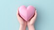The photo shows a pair of hands holding a pink heart against a blue background