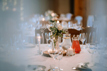 Valmiera, Latvia - August 25, 2023 - Close-up view of wedding reception table with a floral centerpiece, lit candles, and drinks on a white tablecloth.