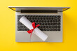 Online education milestone theme. Top view of laptop and diploma scroll on yellow surface with space for message or advertisement